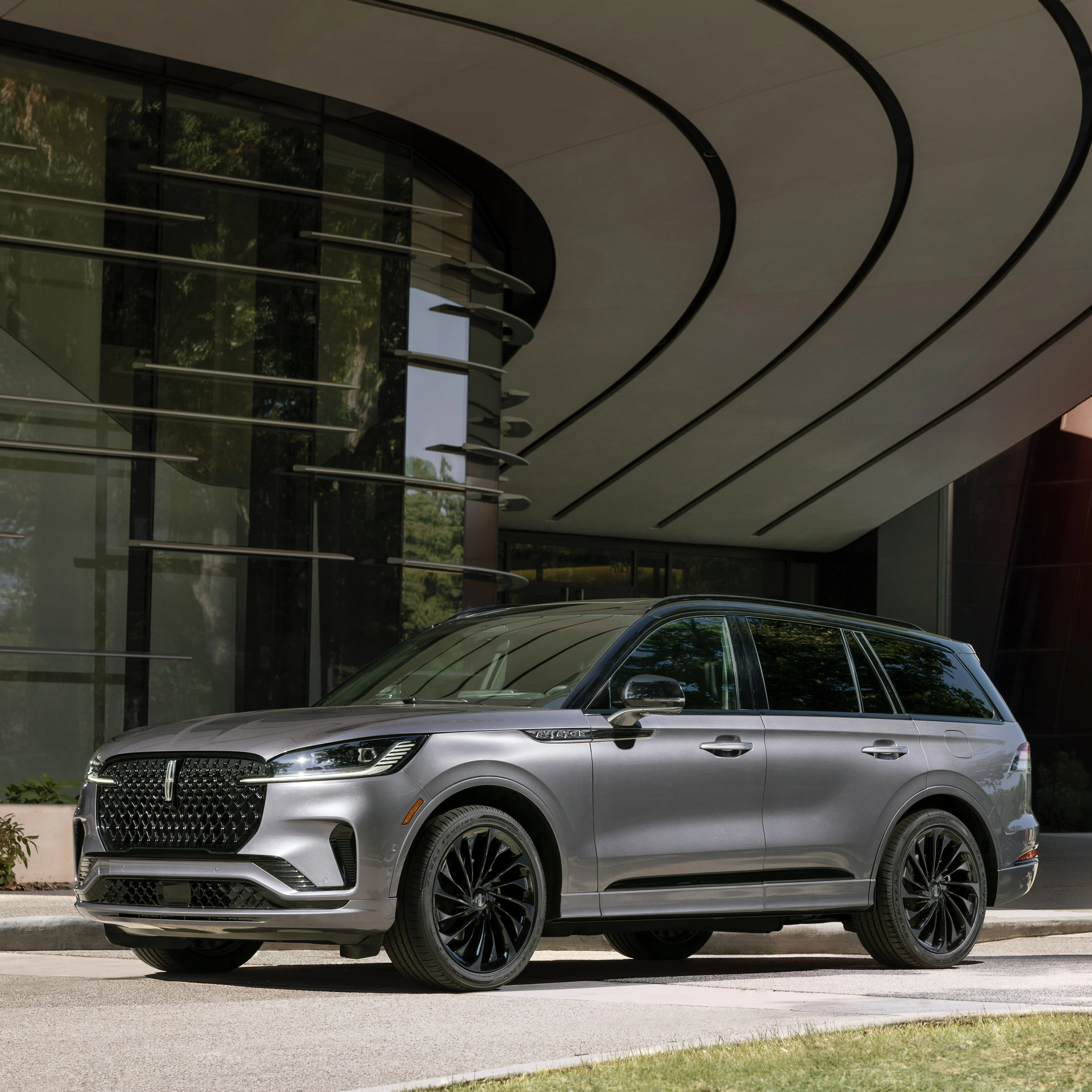 Silver luxury SUV parked in modern architectural driveway with curved overhang