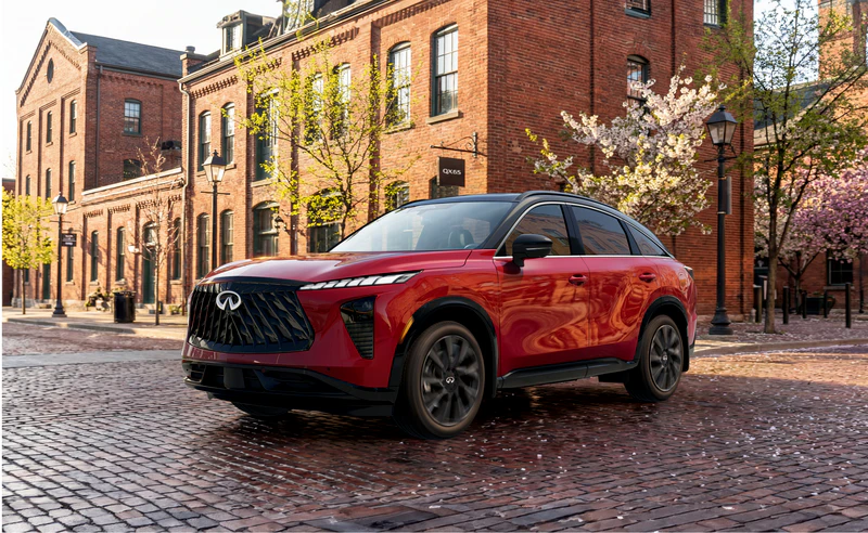 Red Infiniti QX65 parked on brick courtyard in front of historic brick buildings with spring blooms