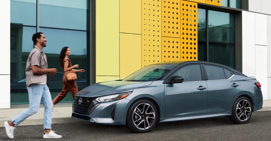 Couple walking past a silver Nissan Altima sedan parked outside a modern building