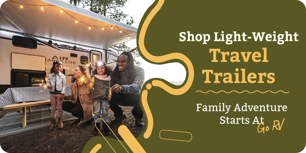 Family standing outside light-weight travel trailer with awning and string lights
