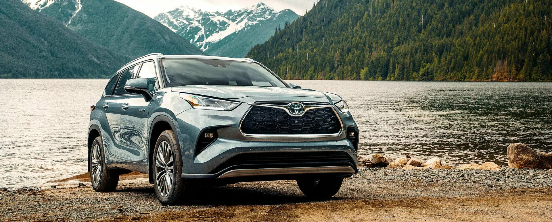 A blue/grey Toyota Highlander parked in front of lake with mountains