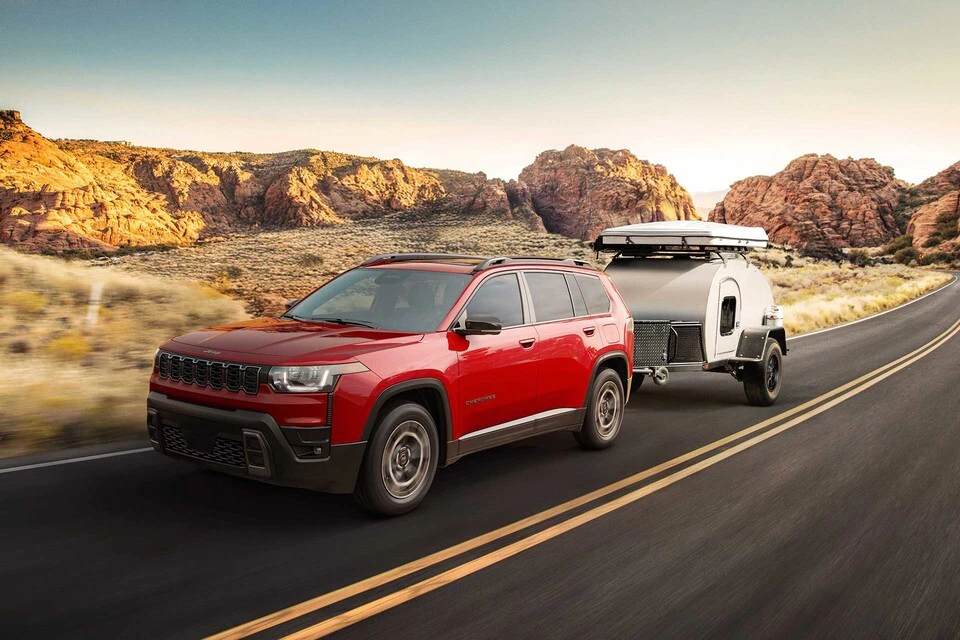 2026 Jeep Cherokee towing a white travel trailer through desert landscape