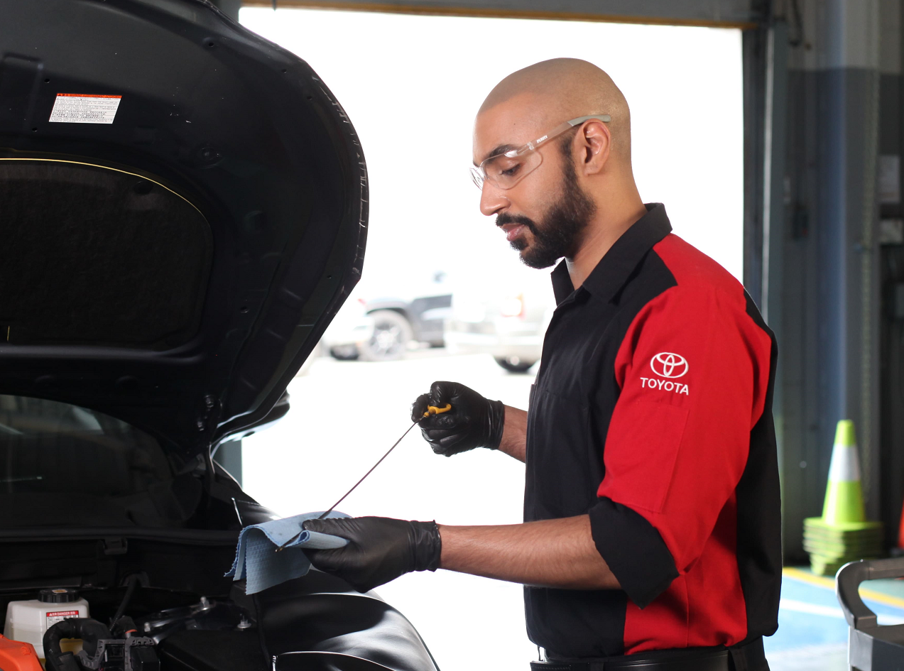 Toyota technician servicing a vehicle. He is wearing classes and cleaning something in his hand. He is wearing glasses and gloves.