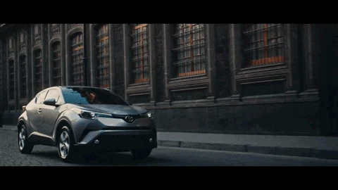 Grey Toyota C HR driving beside an old building. Moody and dark