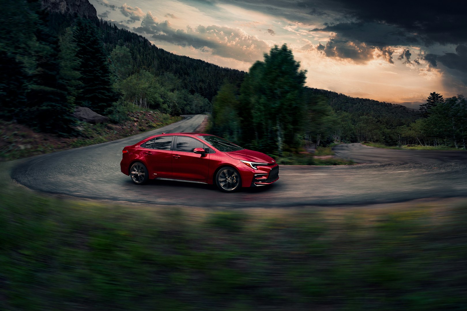Red Toyota Corolla driving down road during a gloomy day