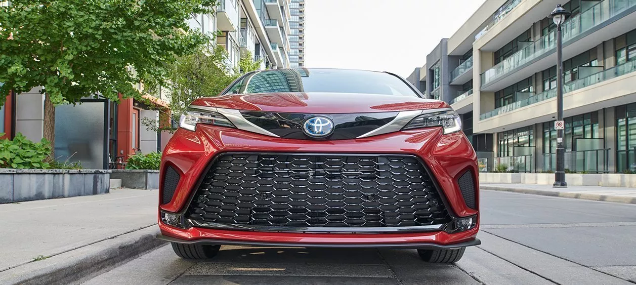 Front facing view of a red Toyota Sienna driving own a road in the city during the day