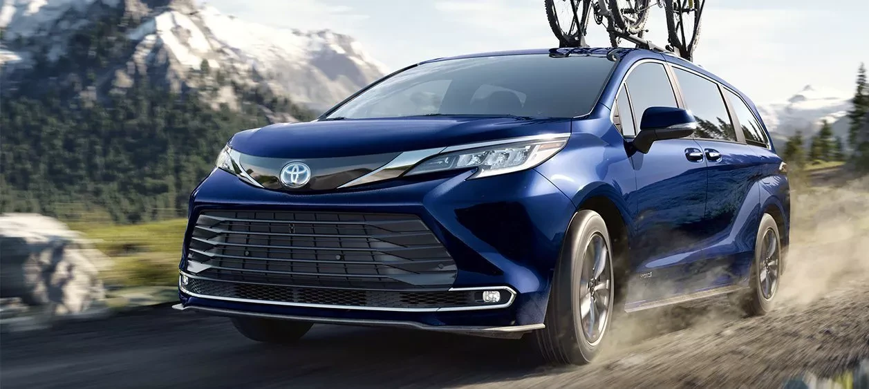 a blue Toyota Sienna driving to the mountains with a bike attached on top of it
