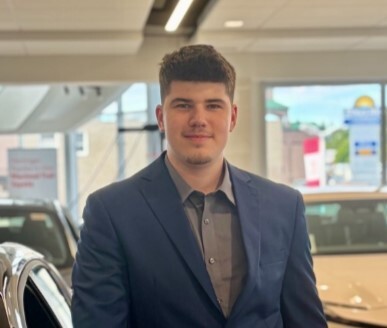 Dealership staff member in business casual attire standing in car showroom