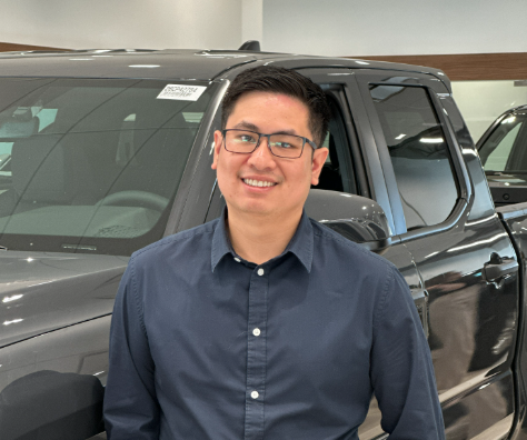 Macleod Trail Toyota team member smiling at the dealership, standing in the showroom beside a black truck.