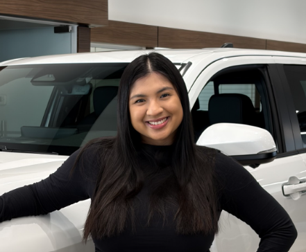 Macleod Trail Toyota team member smiling at the dealership, standing in the showroom beside a white vehicle.