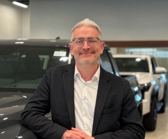 Sales professional posing in car dealership showroom with vehicles in background