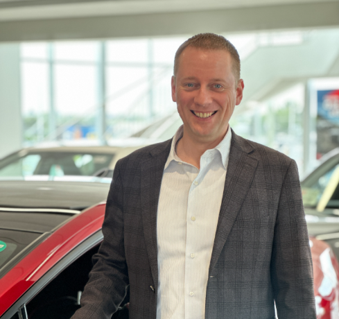 Macleod Trail Toyota team member smiling at the dealership, standing in the showroom beside a white vehicle.