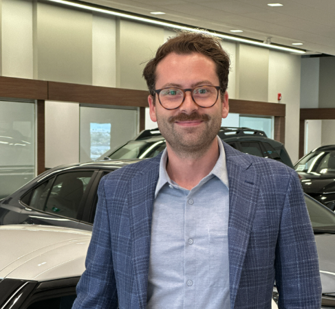 Macleod Trail Toyota team member smiling at the dealership, standing in the showroom in front of multiple vehicles.