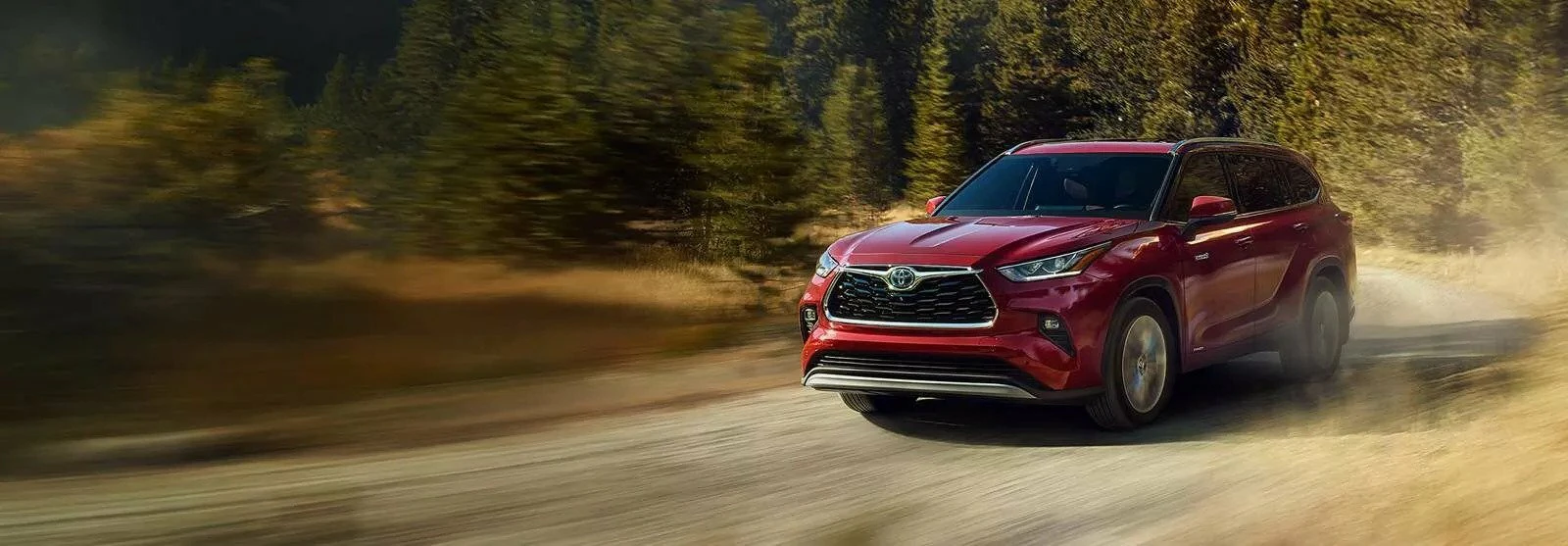 A red Toyota Highlander driving down a dusty road with trees in the back