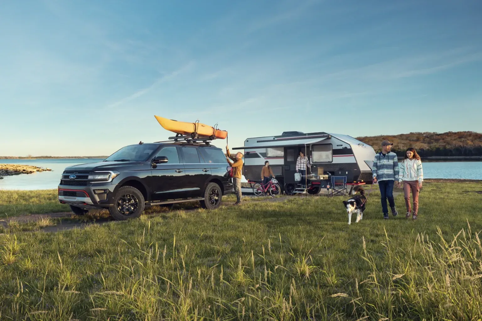 Ford Expedition towing travel trailer with family and dog at lakeside campground