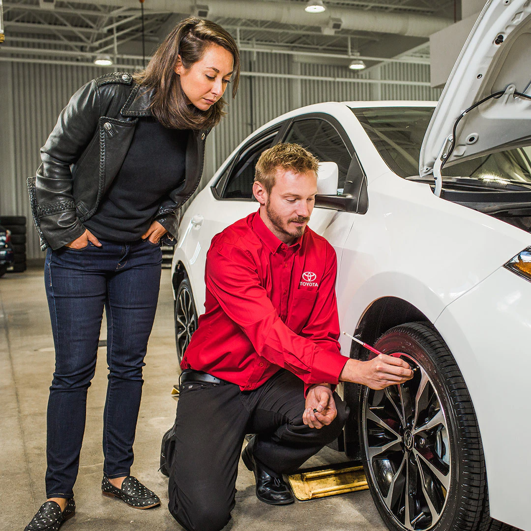 Toyota service technician inspecting tire while customer watches in dealership service bay