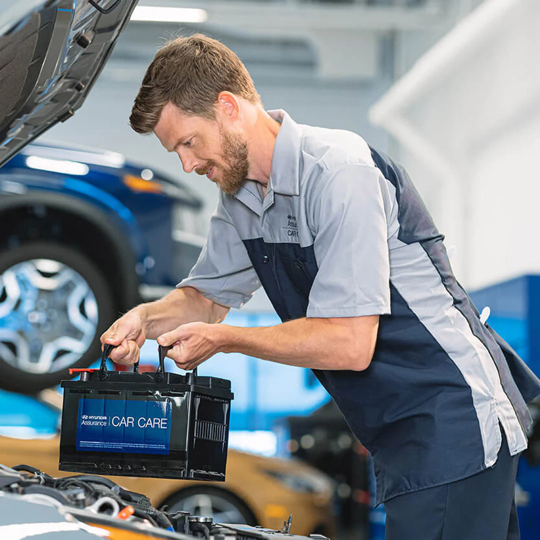 Service technician installing a Hyundai car battery under the hood