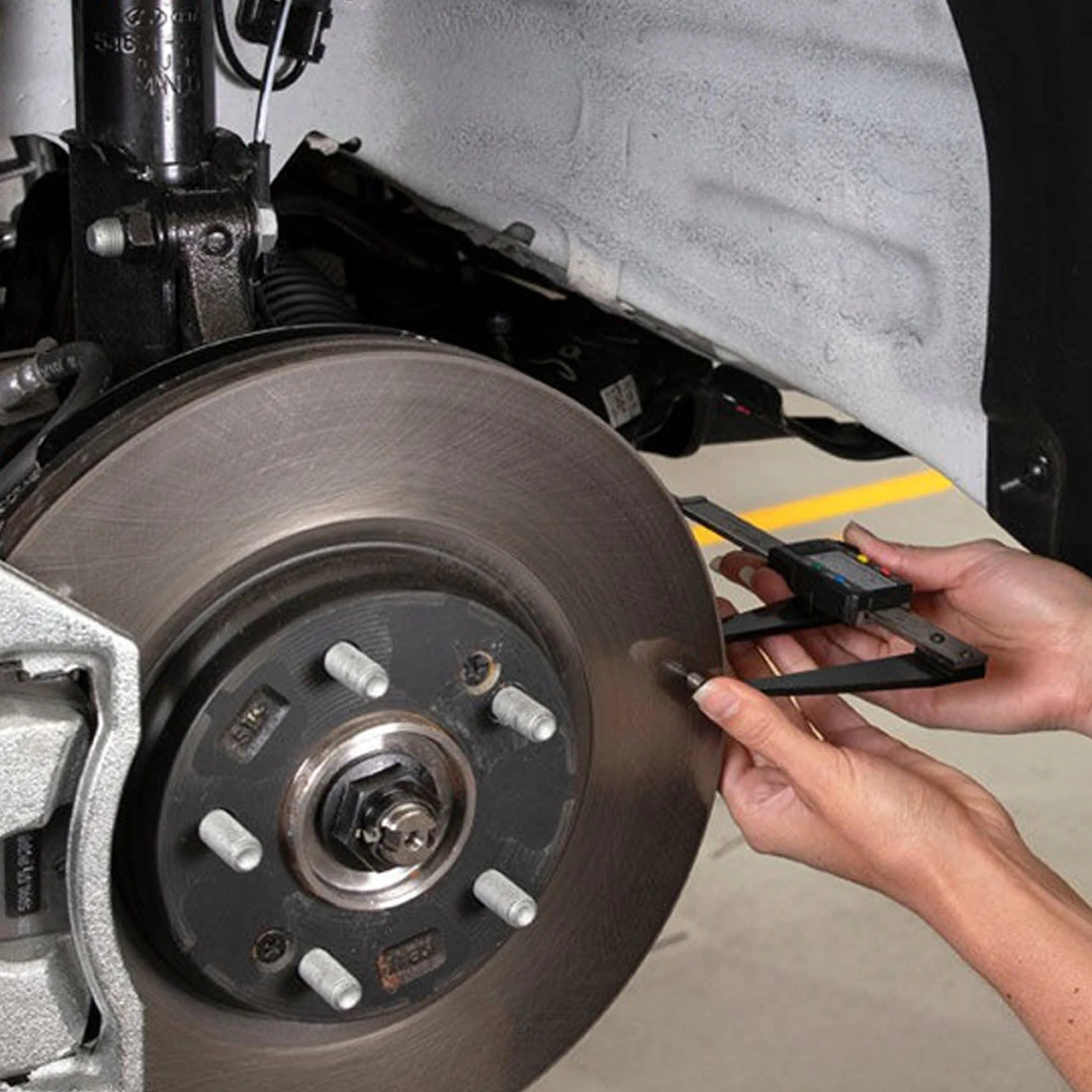 Technician measuring brake pad thickness on Hyundai vehicle rotor with digital caliper