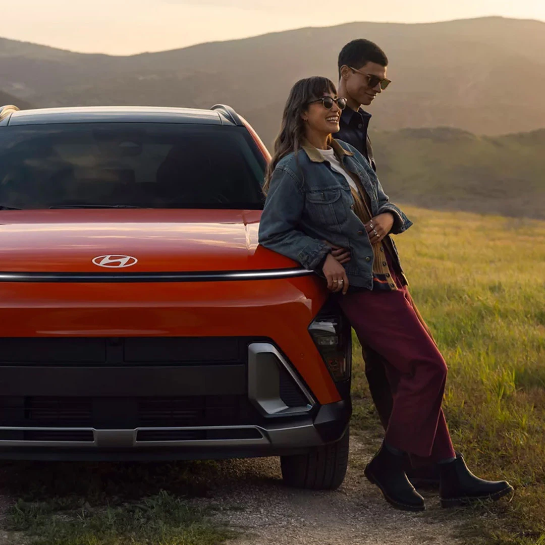 Couple leaning against a red 2026 Hyundai Kona in a scenic mountain valley landscape