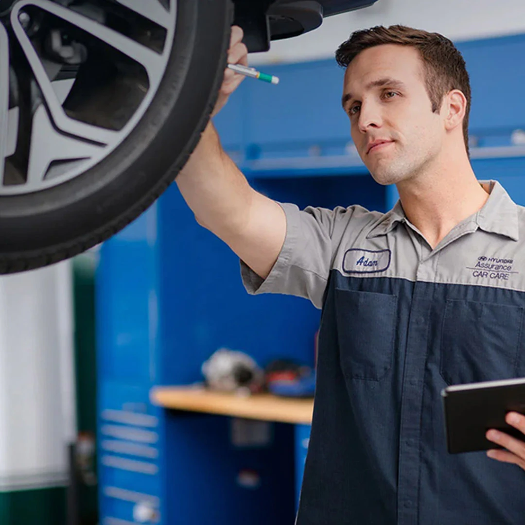 Service technician inspecting a vehicle wheel alignment with diagnostic tablet