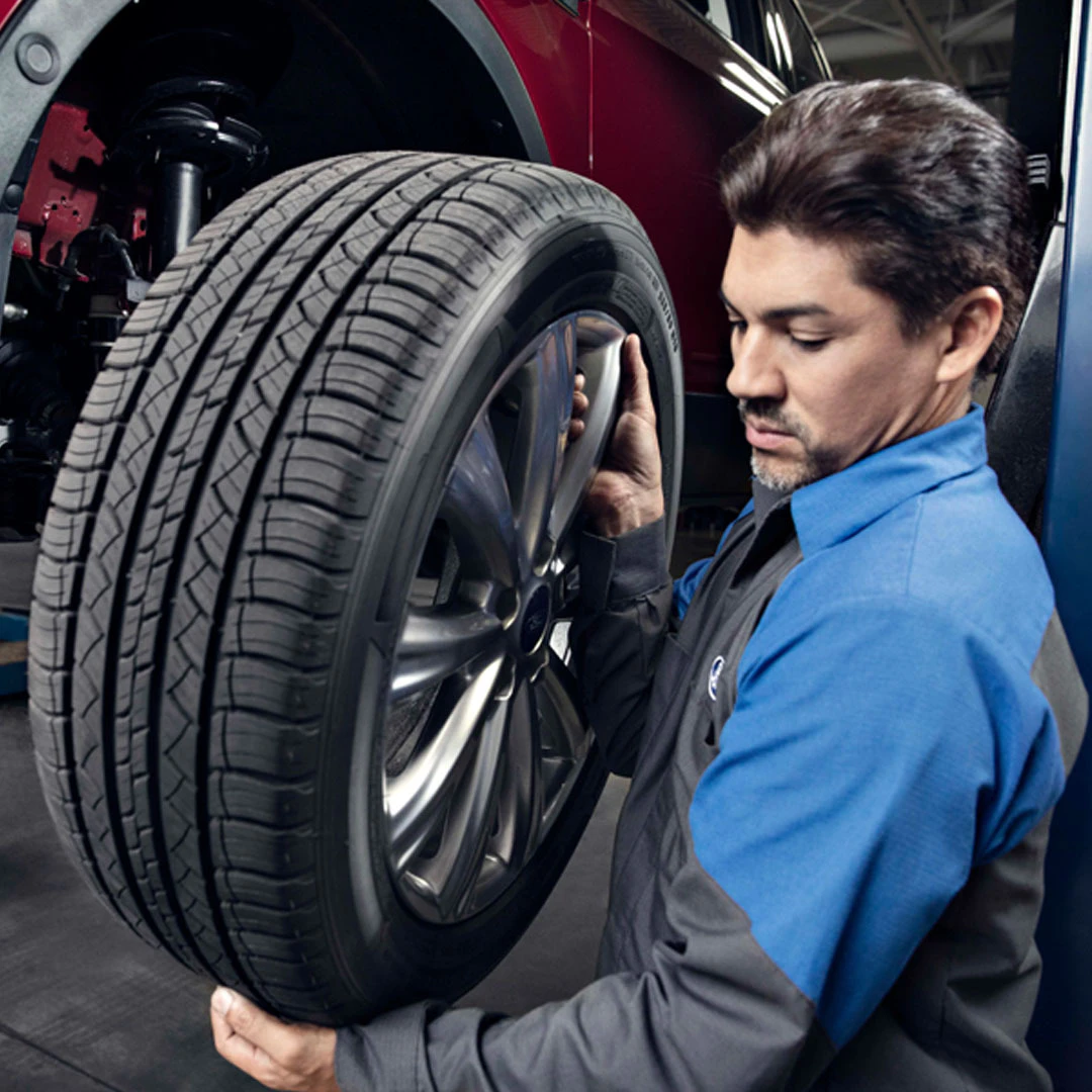 Service technician inspecting tire tread on Ford vehicle wheel