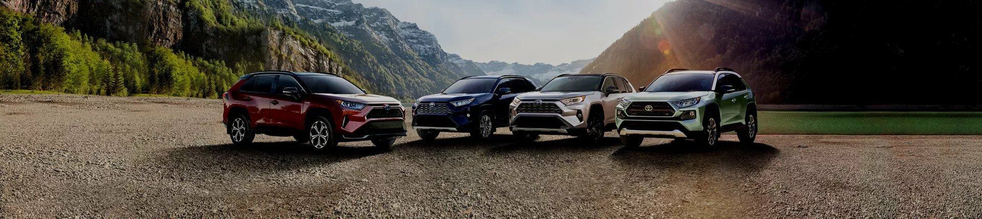 a lineup of four 2023 Toyota RAV4 Hybrid vehicles. They are in front of a mountainous landscape.