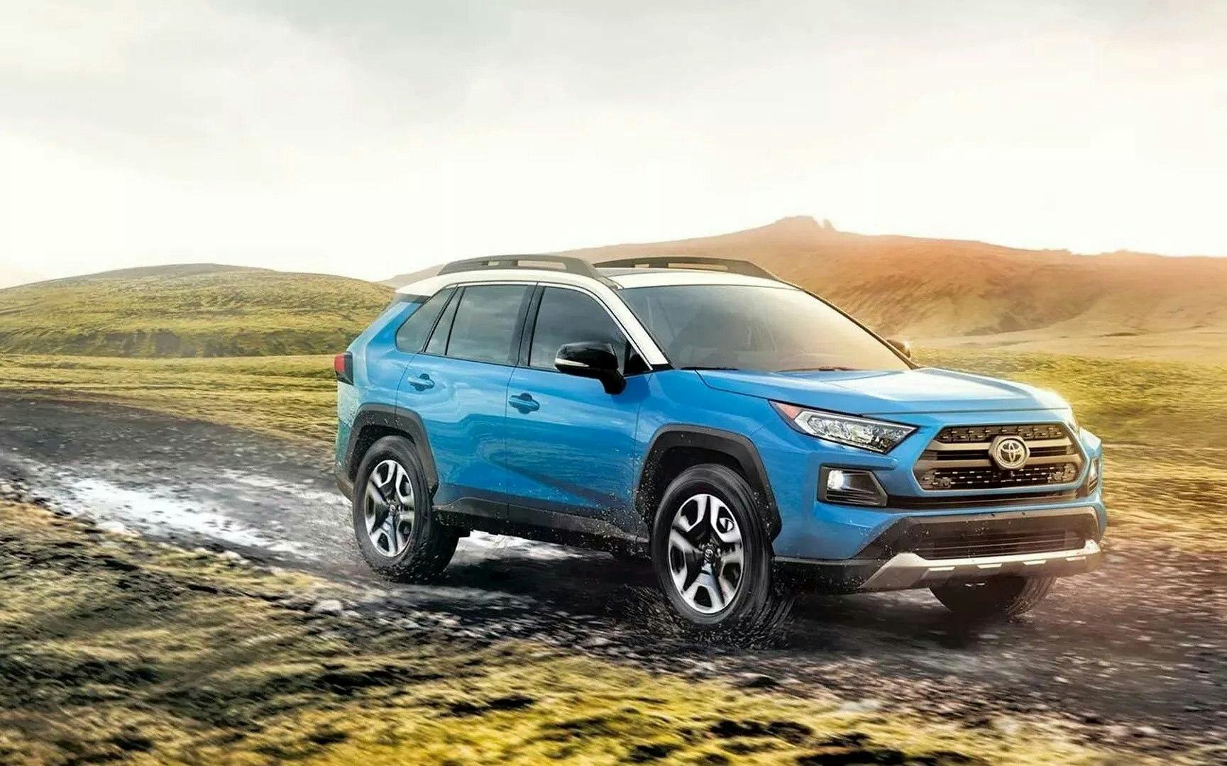 a blue 2023 Toyota RAV4 driving down a grassy and hilly area